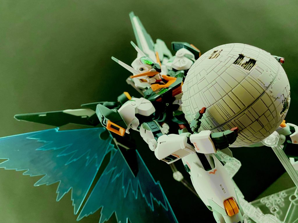 グエル「スレッタ…、スレッタ・マーキュリーっ!」 何度も何度も、呼ぶ。しかし、返事はやはりない。そのエアリアルのコクピットの中は、機体と同じように、虹色の結晶に覆われている。その中に、虹色の結晶、パーメットの結晶に包まれるスレッタの姿あった。それを知ってか知らずか、グエルは叫ぶ。グエル「しっかりしろ、目を覚ませ、そんなんでミオリネを抱けるのかよ!…お前がそんなんだったら、ミオリネは俺が獲っちまうぞ!」 その時だ。エアリアルの瞳に光が灯る。エアリアル自体がまるで意思があるかのように、その身をブルブルと震わせると、その身の結晶を剥がし落とす。元の姿になったエアリアルは、クワイエット・ゼロに向け、払うように腕を振る。振り払った腕から拡がり放たれる虹色の光。その光に触れたクワイエット・ゼロの大部分を構成するリングユニットが、エアリアルが腕を振るうたび、部品単位でバラバラに分解されていく。 やがて、中心部、ミオリネのいる球状のコアユニットだけになったクワイエット・ゼロを抱きかかえるエアリアルは、その背に両の羽を、機械の翼と、光の翼を広げ、その身を虹色の光に包まれながら、静かに、ゆっくりと、地球へと落下、…いや、降りていく。グエルは、それをただ見ていることしか出来なかった。 虹色の光。その帯の中、四肢を失った黒いファラクトが浮いている。…そのコクピットハッチは開いている。 真っ暗な闇の中、ミオリネは一人、膝を抱え浮いていた。先程まで、クワイエット・ゼロの状態を表示していた小さなモニターも、何回かのアラート表示の後、その光を消してしまった。今、自分のいるこの構造体が地球に落下するのだということは知っている。それに対しての恐怖心はない。ただ、「こんな形で、地球に行くのは嫌だな」 暗闇の中でミオリネは静かに目を閉じる。…閉じた目の中に、ぽつり、と虹色の光の粒、それはみるみるうちにその数を増やし…、目を開けたミオリネの前に飛び込んできたのは、無数の虹色の光の粒で形作られた。スレッタ・マーキュリー。 その光のスレッタは言う。「あの」時のように手を差し出し、「助けに来ました。ミオリネさん」