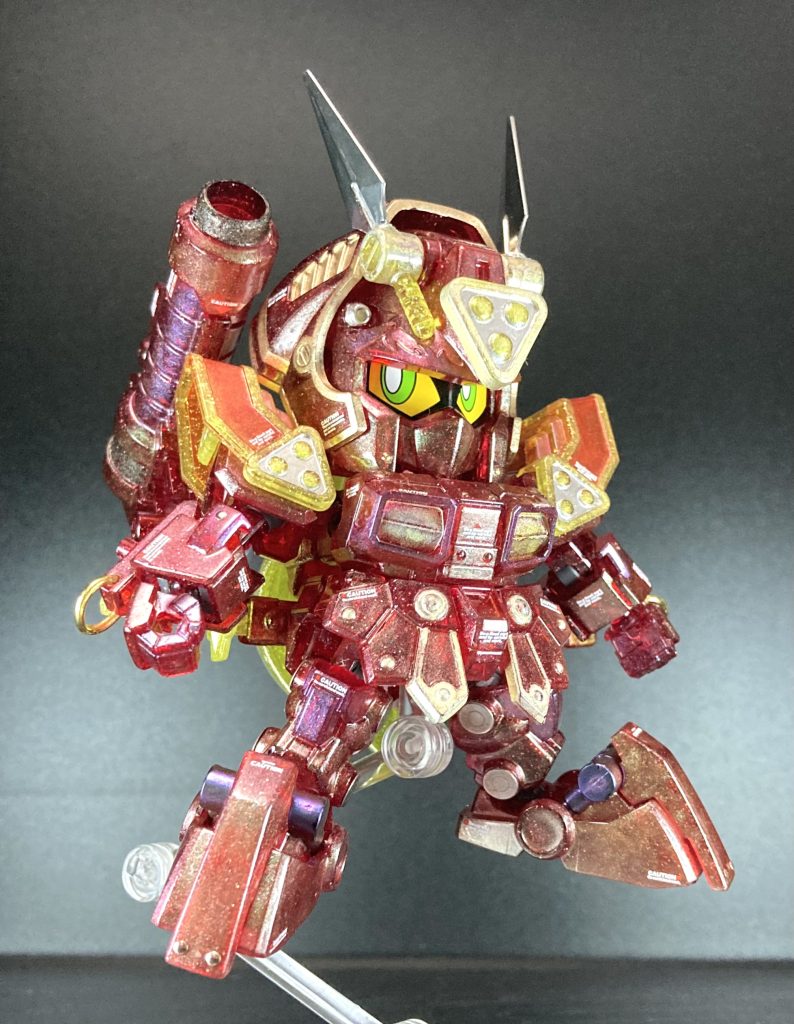 正面から一枚紅武者の成形色がラメ入りクリアレッドとラメ入りクリアイエローの2色やけど、設定配色を再現するために塗り分けてるねん。クリアレッドには基本色の赤部にミラーパウダー緑を塗って,設定配色で暗めの赤部にミラーパウダー紫で塗り分けて、クリアイエローにはミラーパウダー金を塗ってるで、黒部は黒塗りしてミラーパウダー紫を刷り込んだり,銀色やミラーパウダー紫に置き換えたりしてるで。ちなみに、当初のホロ表現の名残が頭部のクナイに残ってるんや… 刃部はメッキシルバーで塗ってるで。