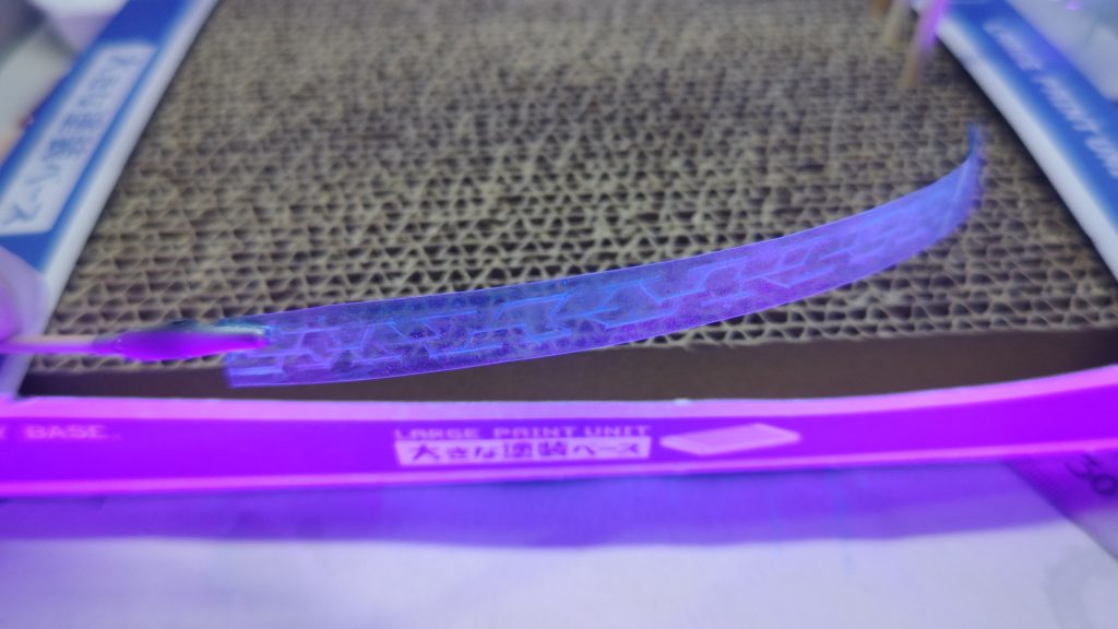 こちらの加工は上の方に書いたとおりあおな@RUBY ROSEさんのX(Twitter)投稿を参考にしています。ただ動画に出ていたセリアのハードケースが見つからなかったので以下の方法で自作しました。1．0.2の透明プラ板の片面にガンダムマーカーエアブラシで「ガンダムマーカーEX 月光蝶 ホロシルバー」を吹きつけキラキラの透明プラ板を作成しました。2.それを細切りしてガンダムマーカーを吹いた反対側にタガネなどでガンビットの軌跡を掘って行きます。3.その後、掘ったスジの部分にガイアの蛍光エナメルのブルーを流し込みはみだした部分はエナメル用のシンナーで拭き取ります。4.最後にスジボリした面にクリアブルーの塗料を吹いて完成です。ただこれは動画にあるようなセンスのあるスジはなかなか根気がいりますので皆さん覚悟してくださいｗ私には無理でしたｗ(ごまかしてある)