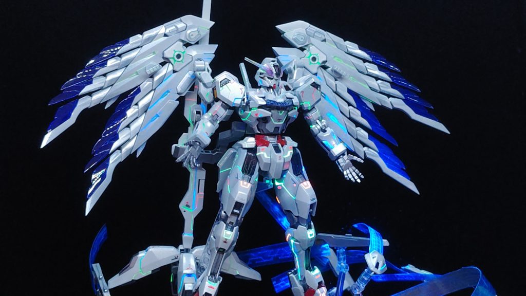 塗装に関してはフレームなどのグレー部分をシルバーで、黄色パーツはゴールドに、赤い部分はメタリックレッドで、そして白い部分はパール塗装で仕上げています。初のパール塗装でしたが思ったよりは綺麗にできたと思います。スミ入れ部分はきこりの切り株派さんのガンダムキャリバーン”Full Parmet”を参考にさせていただきました。爪楊枝は使用しませんでしたが100均で買ったネイル用の筆を利用してガイアノーツのエナメル塗料で墨入れを行っています。翼部分はコトブキヤさんのヘヴィウェポンユニット34 ウイングエッジを2つ使用しています。後述しますがこのキャリバーンはプラモ屋さん主催のフォトコンテストに参加するために組んでいたのですが組み立て途中に寄ったお店でウイングエッジを見かけてこれだ！と思い購入しました。購入後、組み立て説明書を見て複数連結できることがわかったので追加でもう一つ購入し現在のイメージが固まりました。また、平手に関してはミラソウル社製フライトユニットの平手を使っています。