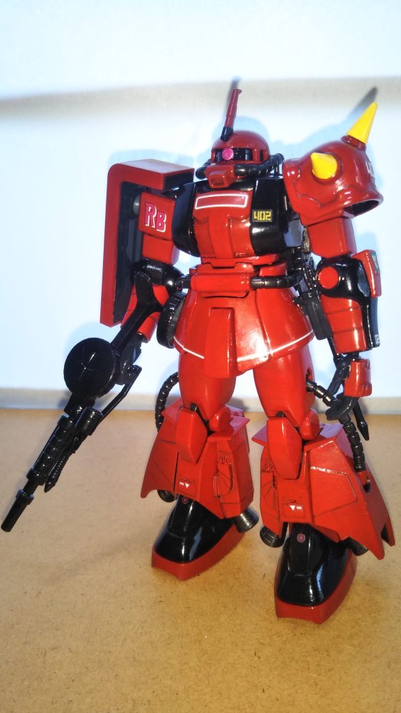 　正面素立ちです。　使用したキットはHGUCの「ジョニー・ライデン専用ザク」です。　基本塗装はツヤ有り赤とツヤ有り黒です（どちらも水性ホビーカラー）。　キットの成形色はシャア専用ザクの色を若干濃くしたようなサーモンピンクに近い色だったのですが、「ジョニー・ライデンの赤はもっと暗い。血の色だ。それと（RBの）マークは右肩だ」と私の中のキリコ・キュービィがささやいたので、下地をツヤ消し黒で塗った上から赤を塗装しました。　かなり理想的な「赤」になってくれたのですが、写真だと照明の関係でやや鮮やかすぎるように見えてしまいます・・・。　関節や動力パイプなどは黒鉄色、シールド裏や手首はミッドナイトブルー、ショルダーアーマーの黄色は水性ホビーカラーのイエローです。　ちなみに、スミ入れはいつも通りシャープペンを使用しています。