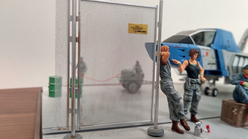 金網は最初目の細かさを間違え網戸にしか見えず、つくり直しました。最終的に看板つけてそれっぽく仕上がったかと。奥には48分の一のフィギュアを置いています。空気遠近法っぽくならないかと少し白めに塗装。