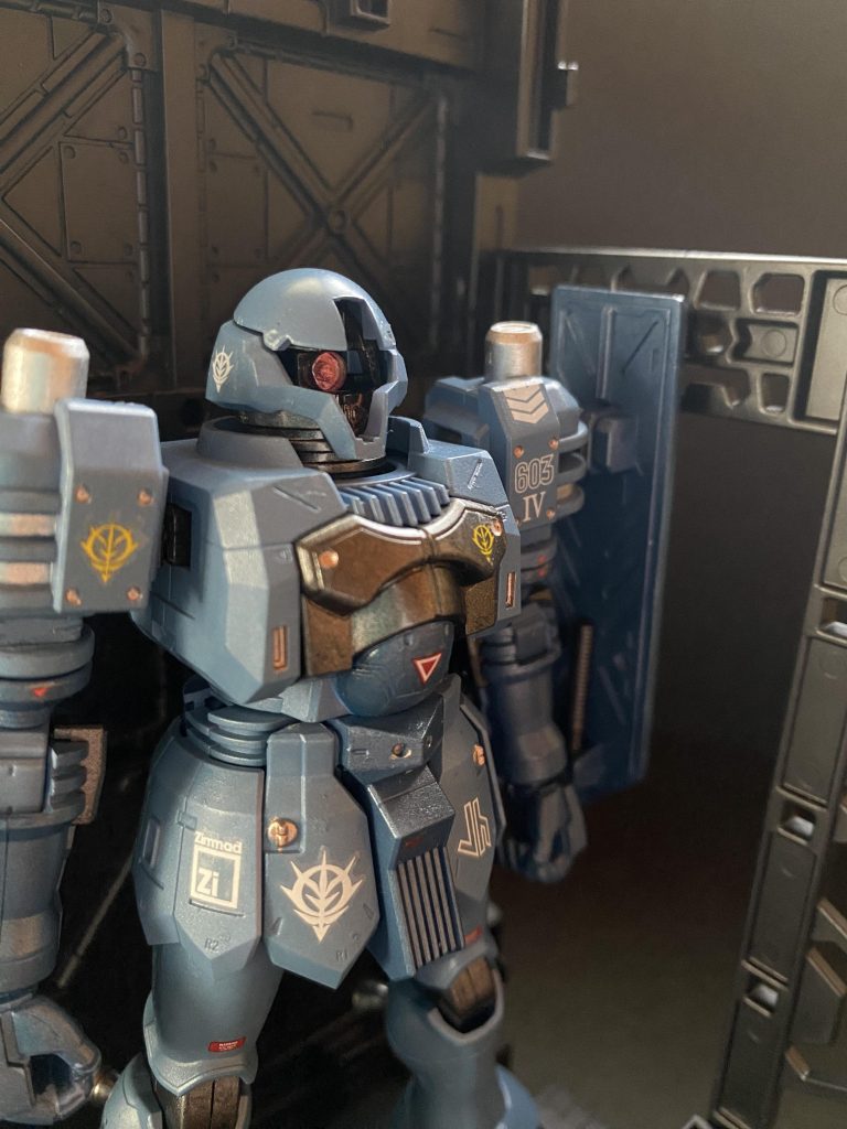 一応モニク・キャデラック特務大尉の駆る予備機という設定の4番機でデカールなど貼りましたが、カッコいいのでデュバル少佐のパーソナルマークも貼ったり、モノアイレールの造形やツイマッド社らしい十字のモノアイスリットを見せたかったので、中央のバーは付けないスタイルで。機体色は、メタリック調のペールブルーと濃いめの同じくメタリックネイビーで、エアブラシ 全塗装。アニメ本編では機体毎にパターンの異なるスプリッター迷彩が施されているという設定だったので、実は過去に一度シールドだけマスキング+筆塗りにより挑戦したんですが、酷い状態に。今回、全部落として、単一色での塗装としました。