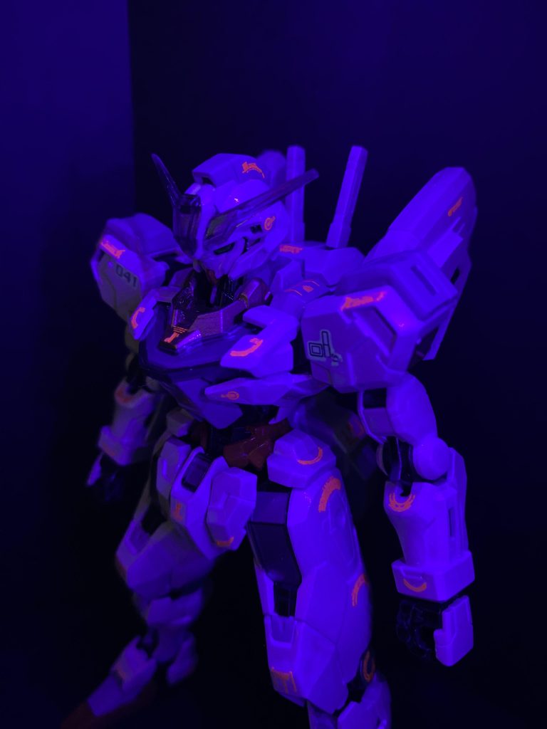 デカールも今回こだわったポイントの一つで、久々に新しいデカールを購入したんですが、様々なバリエーションがあり、最新のデカールの進化にも驚きました。MYKデザインさんのGMコーションデカール No.12 オペレーションテキスト #2 プリズムレッド＆ネオンレッド を使いましたが、よく見る直線的なデザインではなく曲線を主体としたデザインが特徴的で、それがキャリバーンの女性的なシルエットや、魔女の呪文のイメージにピッタリでした。古来、ルーン文字には魔力が宿り、それを身につけることで呪術的な力を得ることも出来ると考えられていたそうです。それを、とある宇宙世紀のサイコなんたらの製造方法と良く似た設定に落とし込みました。また、通常光でメタリックレッドからオレンジに偏光し、ブラックライトを当てればさらにネオンレッドに蛍光します。今流行りのビコーンシステムを、デカールでやってみようという試みです。