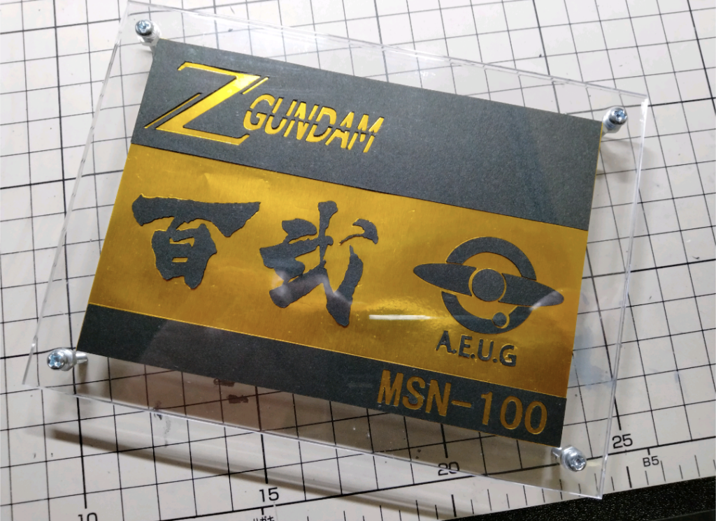 台座は、100均で買った黒い画用紙に、プロッターで文字等を切り出し、同じく100均で買った金色の折り紙に貼り付けて、100均で買った写真立てにネジを脚にして作りました。百式の台座なんで、なんとなく100均にこだわってしまいました（笑）