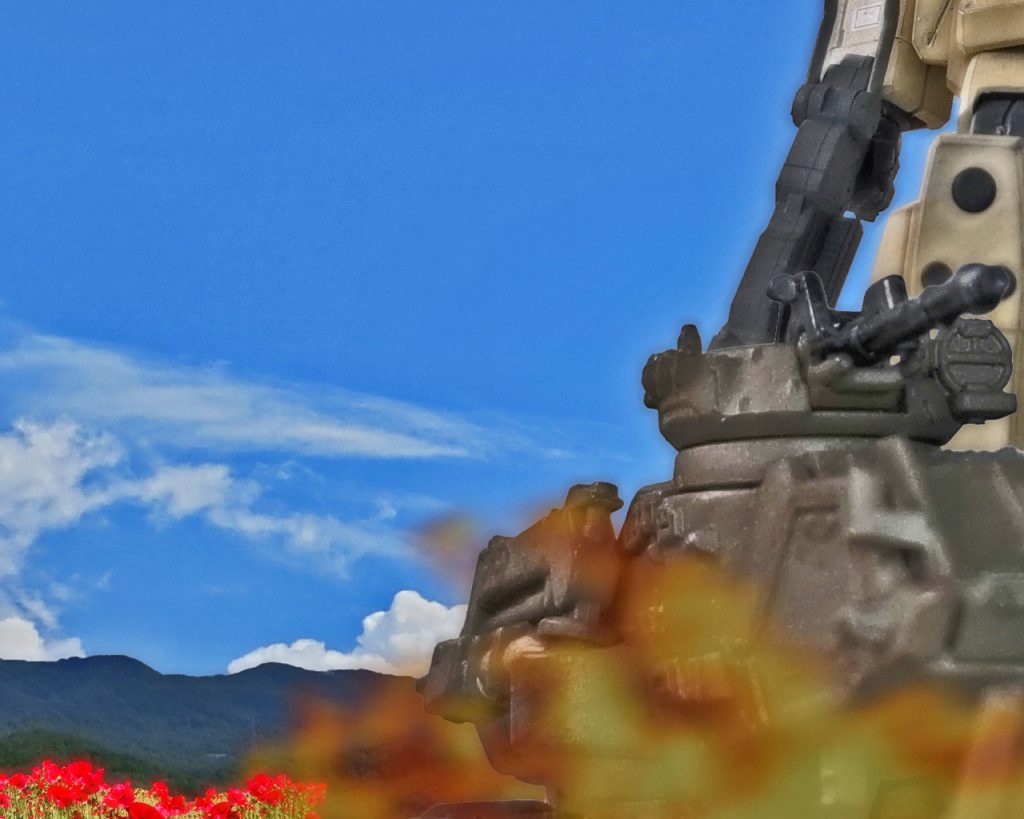 部隊は村の外れにある花畑のある道を進む。「わあ、綺麗。大尉、上開けて良いですか?」「構わんよ」ネスカはモニター越しに見ていた花畑では満足できず直接見ようと頭上のハッチを開けて頭を出した。するとモニターに映るのとは違う鮮やかな花々が視界に入り、優しい香りが辺りを包んでいた。スペースノイドの彼女はこの自然の景色に沢山シャッターを切る。「そろそろ止まるぞい」ニッカードがそう言うとホバートラックは停止し随伴するMSも足を止めた。着いた場所は村の中心部でなく離れた花畑のある広場であった。「ここで到着なんですね」「居住地区まで行くと住民を刺激するからの。ここで良いんじゃよ」全員降車すると大尉と隊の人間は村の管理者と思われる村人と何やら話をし積荷の入替えをし始めた。その間ネスカは別行動をした。