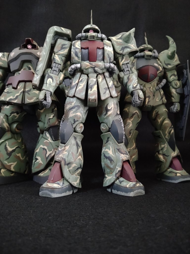 第4中隊本部の所属機、揃い踏みです!コレがやりたかったんです😭いやぁ、おめでたい!何が一番おめでたいかって、やっと破片迷彩から解放される事です🎉🎉🎉さて、以下には、ジオラマに向けた3機に関する諸設定(妄想)を記載します。パイロットの人柄まで設定する必要はないかもですが、暴走しちゃいまして😅もしよろしければお付き合い下さいませ。≪ ジオラマ向け設定(妄想) ≫【基礎設定】・3機は、マ・クベ麾下の虎の子部隊のひとつ、 『第1特別MS大隊』の第4中隊に所属。・第1特別MS大隊の構成は4個中隊からなる。 通常の機械化大隊は3個中隊で構成されるが、 本大隊には特別に第4中隊として、 先行攪乱や陽動、威力偵察を行う中隊を保有。 第4中隊の攪乱後、 第1~3中隊で一気に敵陣を殲滅する意図。 ちなみに1個中隊は3個小隊からなり、 1個小隊は、本大隊では特別にMS4機で構成。 (4機*3個小隊*4個中隊(+各中隊本部に4機)+ 大隊本部に4機=大隊全部で68機!)・その為、第4中隊は熟練パイロットで 固められていた。・第4中隊は象徴的な精鋭部隊である為、 中隊規模では異例の部隊章を認められており、 『デスサイズ(死神の鎌)』を制定している。・また第4中隊は難易度の高い任務を行う為、 敵中で瞬時に味方の識別を行うべく、 独自の部隊カラー(マルーン)を機体の一部に塗布、 同士討ち回避の対策としている。・機体番号は3桁で各桁の説明は以下。 1桁目∶所属中隊番号。 2桁目∶所属小隊番号。中隊本部は0。 3桁目∶小隊内機体番号。隊長機は0。【場所及び時期】 オデッサ近郊、0079晩秋〜0080初夏。【背景】 要衝オデッサは陥落し、 第1特別MS大隊も壊滅的被害を受けたものの、 第4中隊は16機の内12機が残存。 (中隊本部は4機の内、1号機を損失。) なおマ・クベは予め、 万一のオデッサ失陥の対応策として、 秘匿した小規模地下拠点を多数準備しており、 連邦占領地域のゲリラ攪乱を仕掛け続け、 連邦戦力の宇宙への集中を 遅延させる戦力を残していた。 (その戦力の宇宙脱出拠点も一応準備済。。) 殲滅を逃れた第4中隊もこの戦力に合流、 小規模拠点ごとにMSを分散して配置、 継続した抵抗を続けていた・・・。【機体番号400】 階級:大尉 氏名:ルトガー・イーハトーヴ 乗機:MS-06J 設定:34歳。男性。 寡黙だが隊長として果断に富む。 MS操縦の技量は非常に高く、 重力下での運用センスは圧巻。 射撃と近接戦闘、共に絶対的な技量を持つ。 部隊に新型機が配備されてもすぐに部下へ 渡してしまう等、部下思い。口下手であるが その行動で部隊員から慕われている。 始祖は東洋の出身とも。【機体番号401】 階級:大尉 氏名:ヴァルター・オイゲン 乗機:MS-06J 設定:32歳。男性。 MS戦闘に関する技量は高いが 広い視野で現場指揮官としての能力も高く、 後方からの支援と部隊の誘導を担当。 バランスのとれた性格で機転も利き、 副官には非常に適した人物。 オデッサ作戦の熾烈な退却戦で惜しくも戦死。 機体も大破、放棄された。【機体番号402】 階級:軍曹 氏名:クンツ・バウアー 乗機:MS-07B 設定:27歳。男性。 皮肉屋であるが、合理的な性格の持ち主。 小柄で非常に俊敏。近接戦闘では 抜群の成績を収め、模擬戦では ルトガーに勝利する事もある。 好き嫌いが露骨に出てしまう為に 扱いづらい人物であるが、 ルトガーには心酔しており、 オデッサ陥落後も部隊に貢献を続ける。【機体番号403】 階級:中尉 氏名:デニス・アーベル 乗機:MS-09 設定:30歳。男性。 明るく社交的な性格で士官学校時代から 常に成績優秀。上官にも可愛がられるが、 信義に沿わない事へは態度を明確にする 面があり、今ひとつ出世は出来ないでいる。以上です。駄文長文、お付き合いありがとうございます🙇