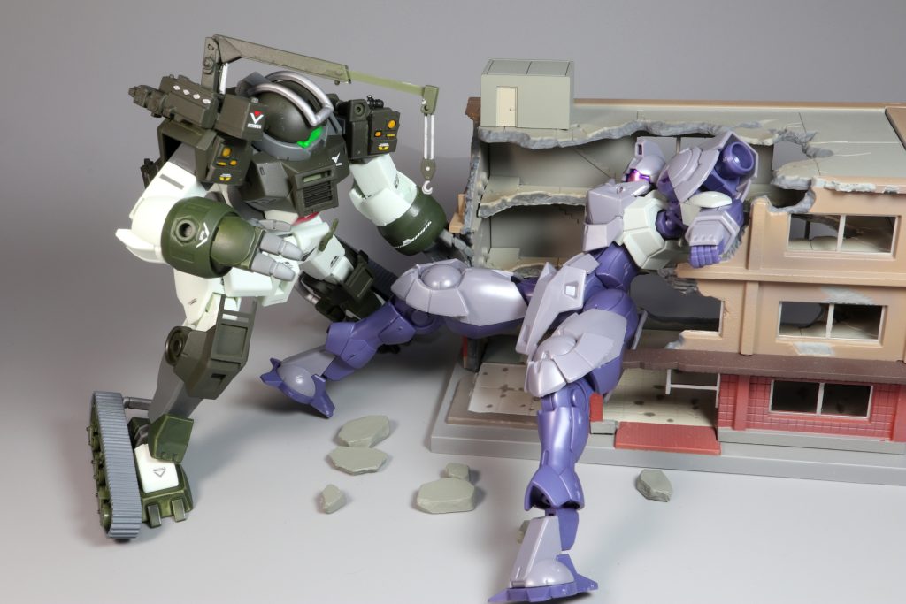 戦闘で撃破されたMSを回収するベルゲ・デミ。主任務であるMS回収を行っています。肩の補助クレーンなども使って再利用可能なパーツ等を回収します。しかし、数十トンの重さのMSがこの様に建築物に食い込んでしまっては取り除くのは容易ではありません。工兵部隊の仲間たちと力を合わせて任務に取り組みます。