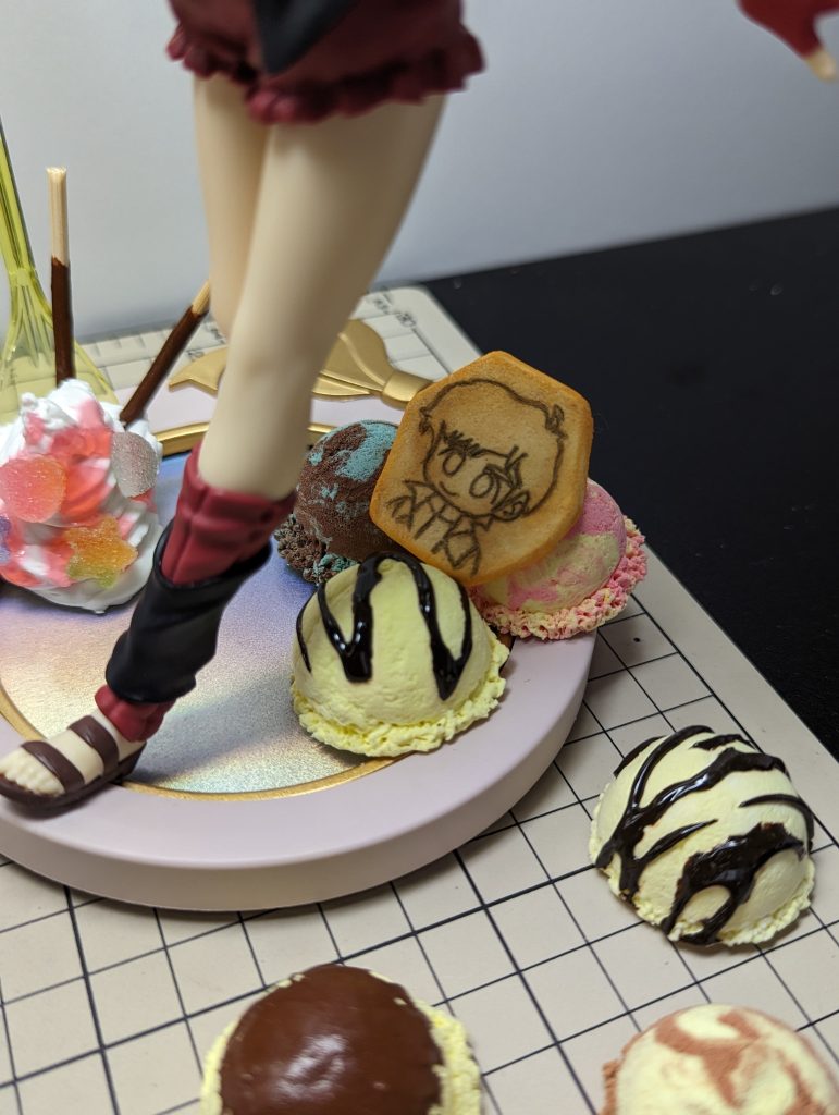 アイスはダイソーの白い紙粘土に、ダイソーの軽量スプーンセットで、小さじと大さじの中間くらいのものを型にして作りました。色もダイソーの絵の具混ぜて色粘土にしています。チョコソースは、木工用ボンドに茶色を混ぜたモノと、ダイソーのクラフト用トッピングチョコソースを使用しています。ジュドーのクッキーも、紙粘土にガンダムマーカーで絵を描いて、タミヤの焼き色マスターで塗っています。