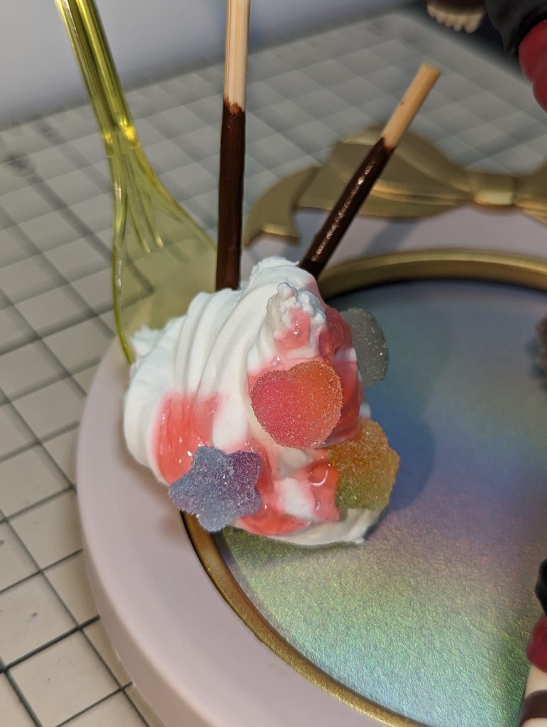 こちらはプラスチックスプーンに、紙を三角に丸めたモノを芯として、周りにダイソーのボンドクリームをお菓子作り用のクリーム絞りで作りました。イチゴソースはトッピング用ソースがチョコとセットになっていたのでそちらを使用。チョコポッキーは、竹串に木工用ボンドに茶色を混ぜてそれを多めに塗りました。飴のような装飾は、ダイソーでこのまま売っていたモノを使用しています。