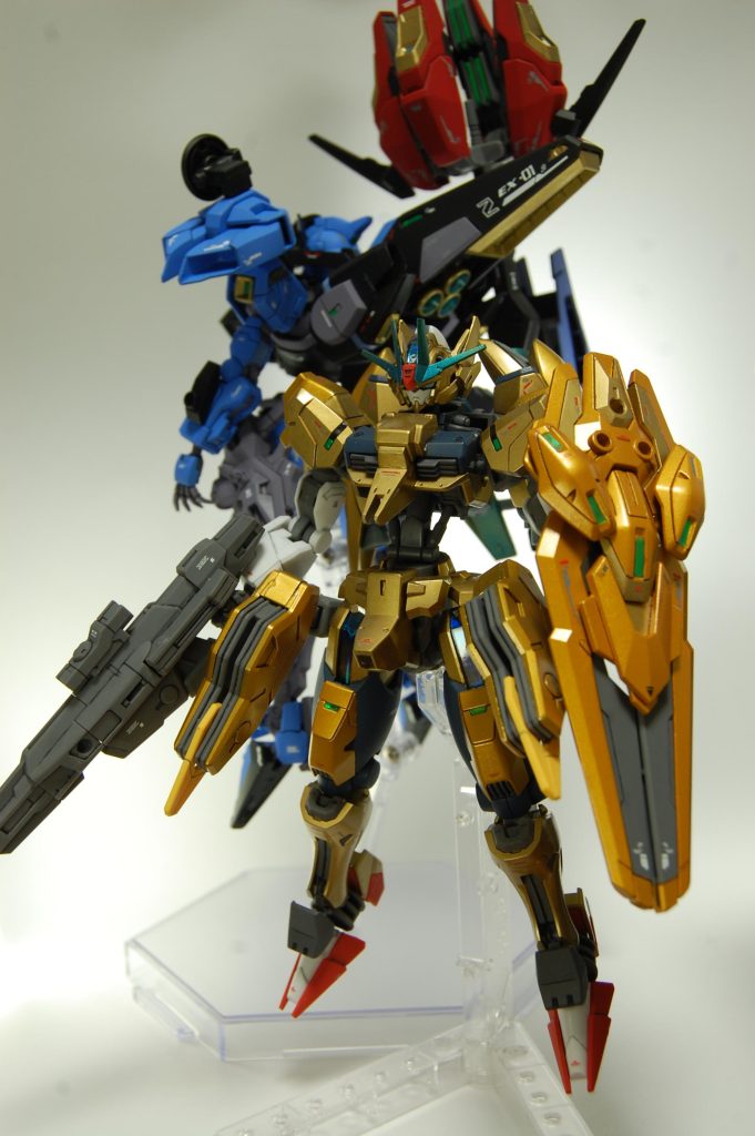 今まで使ったキットの余りのパーツで組みました。基本はエアリアル改修型で、胴とフロントアーマーがアスタロト、バックパックはファラクト、足はエアリアル、アンクルアーマーはデミトレーナーのもので、胸の先っぽと頭部の耳当ては適当なジャンクパーツを切ってくっ付けました。 配色は元祖SDの金色キャプテン準拠+暗めの差し色を入れる方針です。金色はGXブルーゴールドとタミヤのポリカーボネート用のゴールドスプレー、紺色はエアリアル改修型ブルーに黒を混ぜたもの、白とグレーは成形色まま、青緑のメタリックは金色の上にタミヤカラーのブルーメタリックで一部グラデっぽく塗ってみました。金色に寒色系のイメージも混ざって、味方を表してるんだか敵なのかよくわからない配色になった気がします。シェルユニットはセリアの釣り用ホロシールのブルー、各種センサーはダイソーの装飾テープを貼りました。