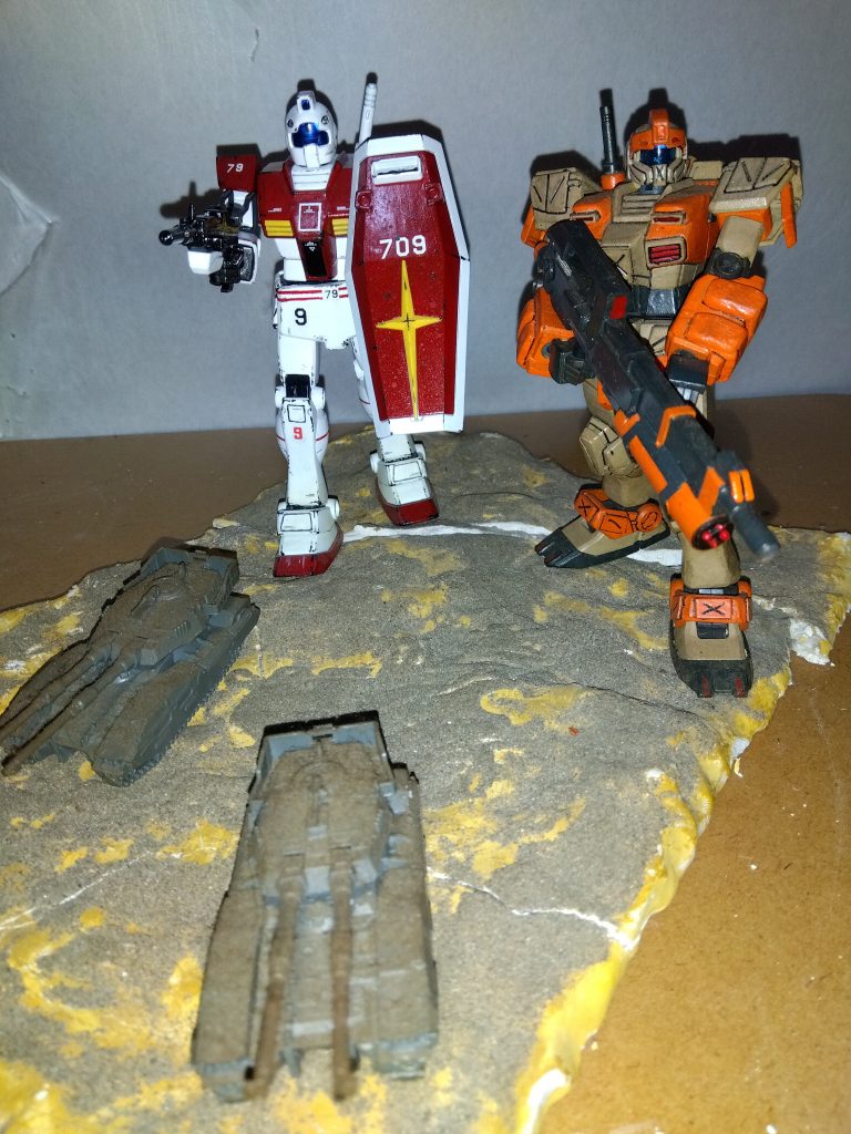 哨戒任務を始めて3日が経過した。 幸いなことに、この3日間連邦と出くわすことはなかったが、夕方にブラックさんがジープを発見した。 ザク・スナイパーのモノアイは強行偵察型のものを流用してあるらしく、こういう時には非常に頼もしい。 隊長がマシンガンで威嚇射撃をするとすぐにどこかへ引き返していったため取り逃がしてしまったが、なんだか嫌な予感がした。 帰投してから基地司令に隊長が報告すると、指令は深刻そうな表情で「そうか、見つかったか・・・」とつぶやいた。「明日の夕方にはHLVの発射準備が整う。 どうかそれまで、連邦をここに寄せ付けないでくれ」司令の言葉に俺たちは緊張感を高めつつも、明日の哨戒任務に備えて基地内であてがわれた宿舎に戻った。 明日は、どうやら連邦と一戦交えなければいけなさそうだ・・・。 翌日、俺たちがいつもの哨戒ルートを回っていたときだった。 ブラックさんが報告を入れてきた。「11時の方向、およそ5キロ先。 連邦です!」とうとう来たか・・・。 全員に緊張が走る。「敵の数は?」「確認できるだけで、モビルスーツが6機、戦車4両。 ただ、幸いなことにこちらはまだ発見されていなさそうです。 ミノフスキー粒子のおかげですね。 先手を打つなら今かと」隊長の質問に、ブラックさんが答える。「よし。 1キロほど先の、あの大岩まで移動する。 私が合図したら、サムは岩の左から、私が右から飛び出して、一気に仕掛けるぞ。 ブラックは岩の上までジャンプして、そこから狙撃してくれ。 軍曹は私の、ピーターはサムの直掩だ」「「了解!」」