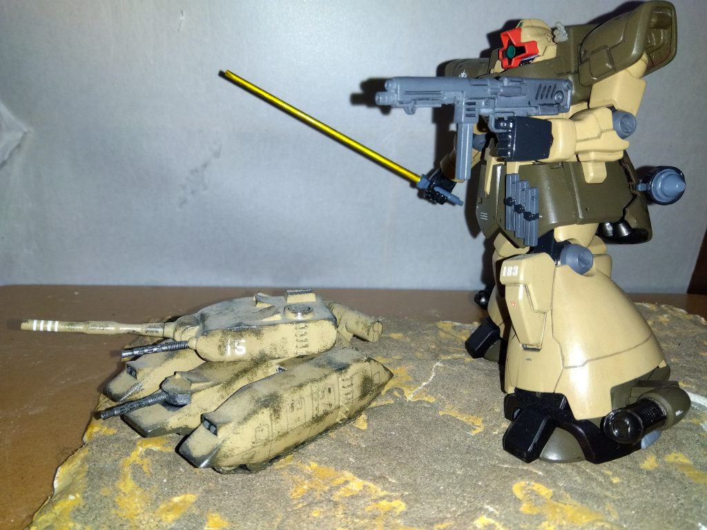 「軍曹、スモークを散布しろ。 敵に接近しやすくなる」「了解。 ただ、こっちも狙いを付け辛くないか?」ハセガワ軍曹が答える。「今のうちに目視で大体の位置は確認できる。 見たところ、敵のモビルスーツはそんなに動きが速くない。 現在位置を頭に叩き込んでおけば大丈夫だ」リリーの答えに納得したようで、M1戦車は砲塔右側に取り付けられたスモークディスチャージャーを展開させる。 リリーもドム・トローペンの左肩に増設されたスモークディスチャージャーを発射した。 あたり一面が白い煙に包まれる。 リリーは素早くドム・トローペンを移動させ、敵の真横から接近を試みた。 予想通り、連邦のモビルスーツはザクと同程度の速度でしか移動できないらしい。 最初に確認した位置とほぼ変わらない場所で明後日の方角へビーム兵器を連射していた。 その1機に、先ほどと同じようにヒートサーベルを突き立てる。「さて、残りは戦車か・・・」その瞬間、煙の中で爆発が起こった。「なんだ? 軍曹が戦車をやったのか?」しかし、インカムにザーッというノイズが混じっていることに気付いたリリーは一瞬で青ざめた。「軍曹!?」