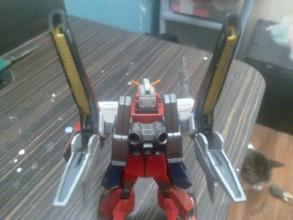 On the custom backpack, are 4 thrusters along with the experimental flight system. These next-generation engines are powered by minovsky compact reactors, one in each. The super high output of this system can generate streams of charged particles from the exhaust. These super hot particles can act as large beam saber blades, slicing through enemy mobile suits and ships.