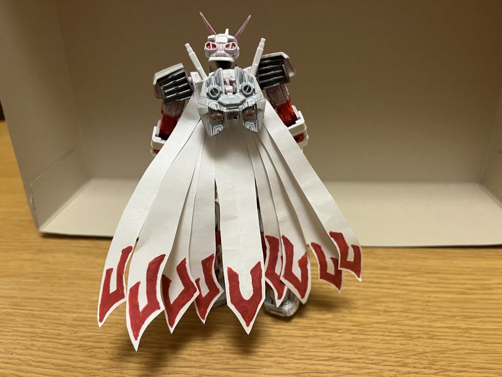 キュウビテール本機の背部に装着された専用マントであり、事象の加速を具現化する機能に加えて、重力操作能力と空間破壊能力も備わっており、これらの性質を併せ持つ巨大な青いエネルギー体を自在に生み出す事も可能。この青いエネルギー体は、最大9本まで使用可能で、空間破壊を攻撃に転用すれば超高層ビルを軽々と一撃で破壊し、重力操作によって引力や斥力などを歪め、敵の攻撃を反射したり動きを遅くする事もできる他、最大本数まで使用すれば要塞や戦艦ですら身動きを取れなくさせる程の拘束力を持つ。本機に創世能力がある関係上、破壊された建物や地面を即座かつ急激に修復したり、負傷者どころか死者までも即座に治癒・蘇生するなど、有機物・無機物の区別なく能力は適用できる他、空間破壊能力と併用する事で、破壊した地面に敵を埋め込んだまま修復し拘束するといった芸当も可能。これらの機能・能力を本機にも適応する事で、超越的な加速を生み出し、フォースインパルスガンダムエクストリームの亜光速レベルに近いスピードを生み出せる他、重力操作による空中を飛行、擬似的な空中歩行さえも可能とする他、ダイナマイトブーストモードとの重ね掛けも可能としており、その際にはフォースインパルスガンダムエクストリームをも上回るスピードにまで到達するが、その分パイロットの負担も大きくなる。