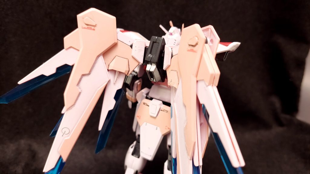 一方でこの設計図では本来ウイングにあったプラズマ収束ビーム砲や腰部のレール砲はおろか頭部機関砲やビームサーベルに至るまで撤去されており、MSとして製造された場合一切の武装を持たない。人類という種のより高次への飛翔を願い、ただ一つ用意された装備がこの立像の象徴たる翼である。また、カラーリングについてはプロジェクトの取りまとめにあたったオーブ代表カガリ・ユラ・アスハに敬意を表し彼女のパーソナルカラーが選ばれることとなった。