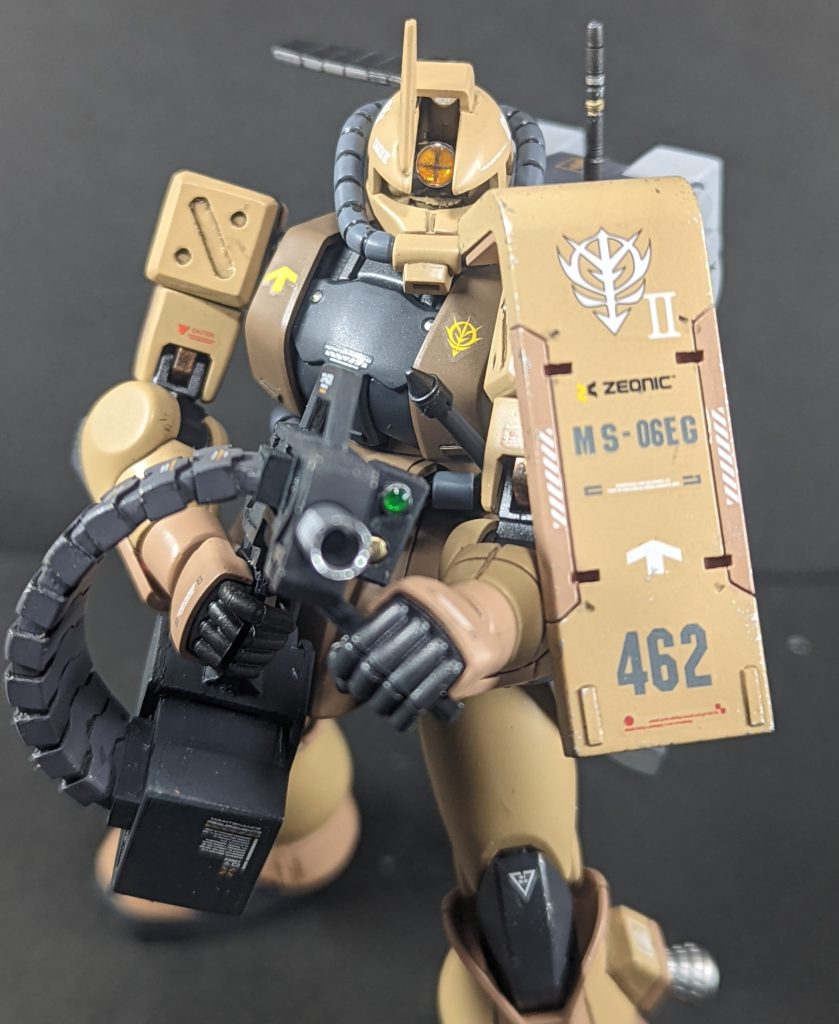 ジオン軍中央アジア方面軍第46小隊所属2番機 一年戦争後期、MS不足のジオン軍では前線でも新型もあまり供給されないので、ザクⅡを改造しながら連邦の高性能MSと渡り合っている。パイロットは小隊の副長だか、小隊長が脳筋突撃馬鹿なので大体の場合作戦立案から作戦指揮まで行っているためやっていることは実質小隊長。その上、偵察や妨害工作の他、狙撃の観測手も行うので、他部隊の味方からは「アイツいつ休んでんだ?」と思われている。小隊長をカバーした結果の負傷の後遺症で片目と片腕が不自由になってしまったが、「俺が退役したらアイツ(隊長)突っ込むしか出来ないから直ぐ死ぬ」ということで小隊に残っている。近接戦闘や精密射撃は出来なくなってしまったため、支援に徹するようザクⅡに改造を行って現在の機体となった。その分、小隊に新兵のパイロットを入れて他の小隊より1機多い4機の小隊編成となっている。本人曰く「怪我の責任を感じてか、隊長が前より言う事聞くようになってやりやすくなった。ただ、今度は新兵のおもりをせにゃならんからそっちの方が頭が痛い。」とのこと。