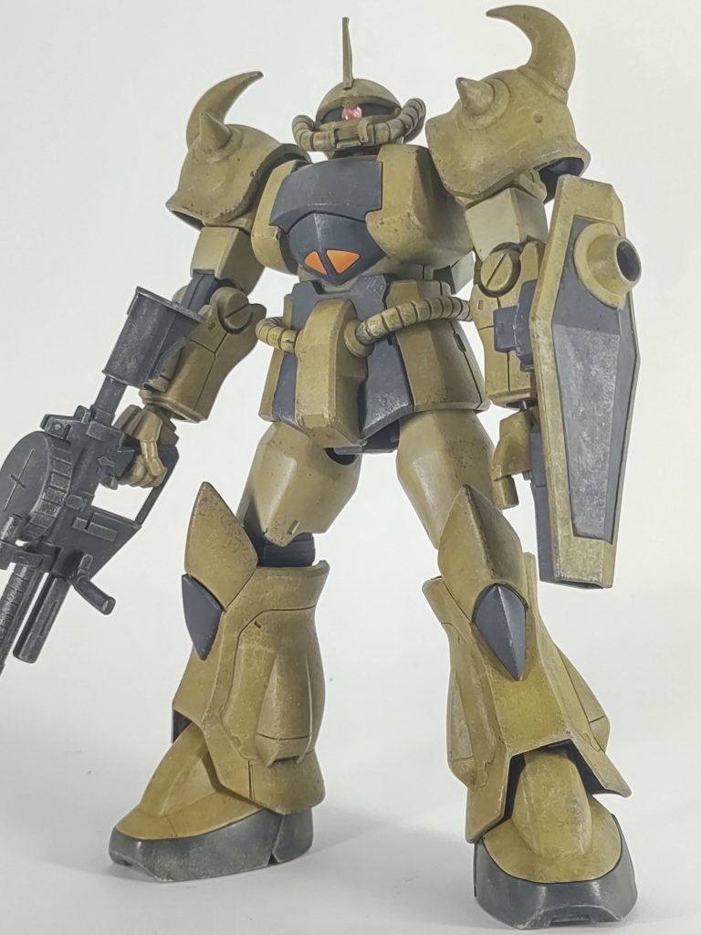 手持ちのタミヤアクリルでなんとかなりそうだったのでデザートカラーにしようと思いガンスタ含めネットでグフのデザートカラーを調べまくったんですが、配色のリファレンスになるようなものがなく、人によって配色がバラバラだったので、だったら自分のいいようにしようとしてこうなりました。以下、自分的記録です。茶色: イエローブラウン(XF-92) → ダークイエロー2 (XF-88)明るい茶(腿、二の腕):  バフ(XF-57)→ バフ+フラットホワイト(XF-2)少々黒: ジャーマングレー(XF-63) → ダークグレー(XF-24)関節: Mr.メタルカラーのアイアン武器: 成型色にガンメタル(X-10)とチタンシルバー(エナメル)のドライブラシランドセル: ニュートラルグレー(XF-53)モノアイ: Hアイズ+ホイルシールの余白(余銀?)で裏打ち全箇所、ベースの一段暗い色をモールドを潰さない程度にざっと塗って(筆ムラ上等)、スポンジポンポン、筆ポンポン、ドライブラシを重ねて表情を作ってから、明るい色でドライブラシ。この上に全体的にフラットホワイトでドライブラシしたんですが、ウェザリングカラーのステインブラウンでフィルタしたら思ったよりトーンダウンしてしまい、その後も軽く明るい色で撫で回しました。あとは恐る恐るダークグレーでチッピング。スポンジチッピング全然上達しない...怖くてすぐギブ。墨入れはしてないです、エコプラの黒い成型色が見えています。ジャーマングレー→ダークグレーはムラ無く塗れてしまったのと色が近すぎてあまり表情出ませんでした。写真だと思ったより光って映っている所もあるんですが(盾とか)、実物はほぼ黒いです。