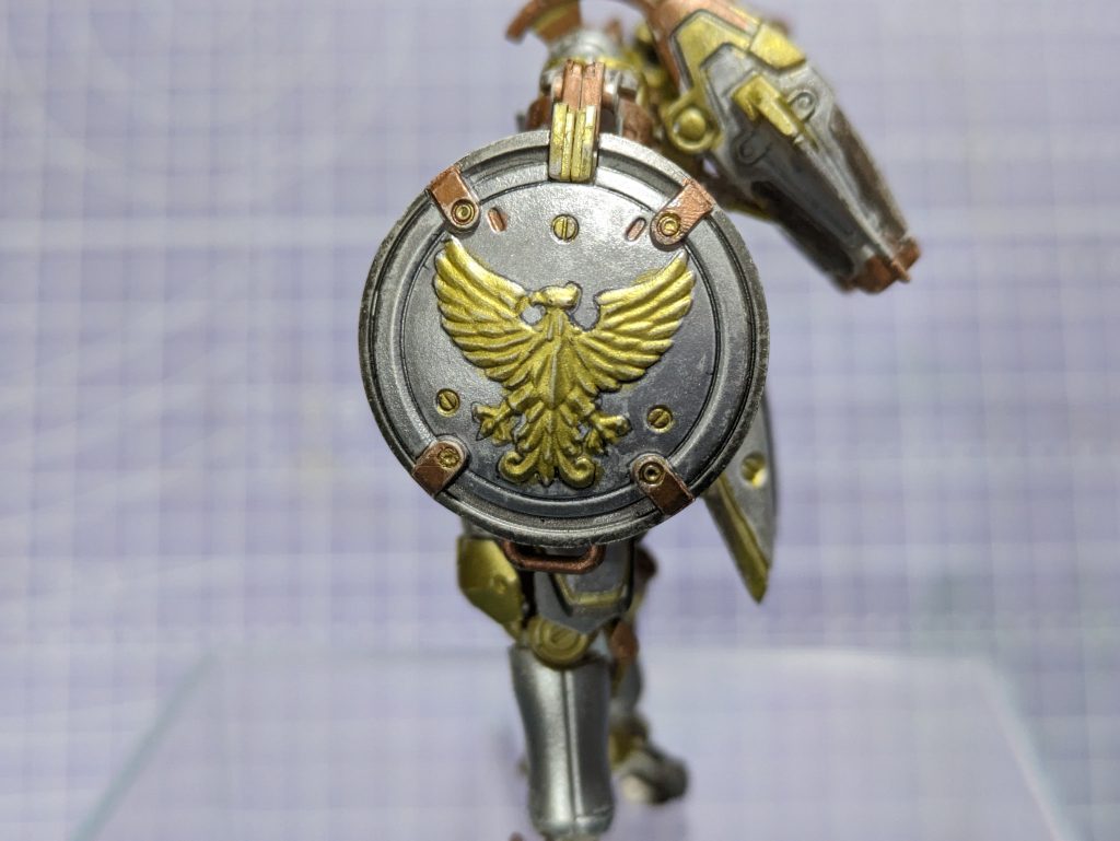 E:おなべのふたならぬバックラーというかラウンドシールドですかね。某製薬会社か世界征服を企む悪の組織のような鳥のエムブレムがとてもカッコ良いシールドです。これは塗ってて楽しかったです。こういう小道具には筆（ペン）ムラが良い感じに仕事をしてくれます。何気に革バンドのような部分がお気に入りですｗ