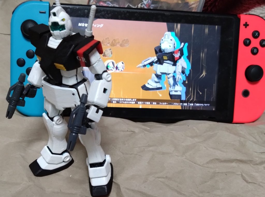 最後に記念撮影。ゲーム『バトルアライアンス』のパッケージとゲーム内のジム(ギャザーロード仕様)との撮影。製作したジムとゲーム内のジムを見比べてみて下さい。それでは！今年も宜しくお願いします。