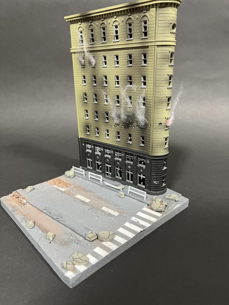 ジオラマベースは市街地をイメージして。量産型ガンタンクの履帯が通過したアスファルトのヒビ割れた表現にこだわってみました。建物は市街地戦の影響で火災が出ているイメージで窓から煙を上げてます。