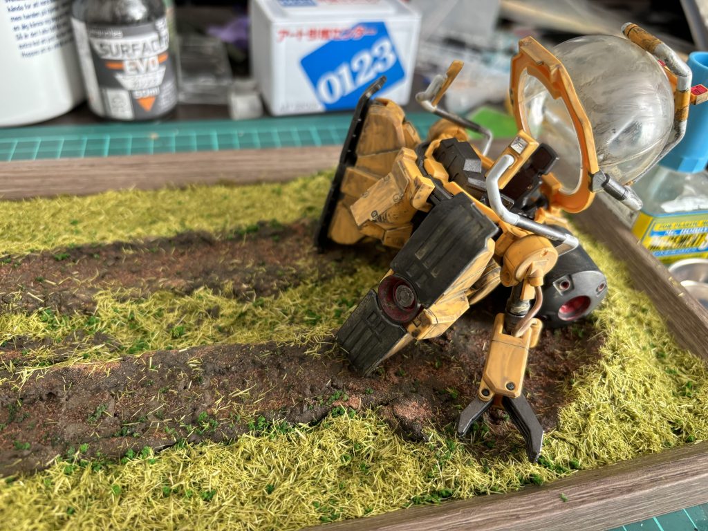 初め、100均素材だけで全部作ろうと思ってたんですが、どうも土の色合い上手く出せる自信がなくて、動画色々みてたら、『ジオラマ用粘土』なるものがあると知り、早速購入。思った以上に土の感じが出ましたw足で引きずった跡はパーツを使って実際に引きずってみたりら足跡のように踏みつけて幅を測ったらしました。芝生と土の境目にはジオラマスポンジ少し撒きつつ、芝生を上からかけて誤魔化してみました。抉れた土部分も元々の粘土の色でも良いかなと思いつつ、ウェザリング塗料を上から塗ってみて、さらにジオラマ用の土表現用の砂みたいなの撒いて粒感あげてみたりできないかなと思いやってみました