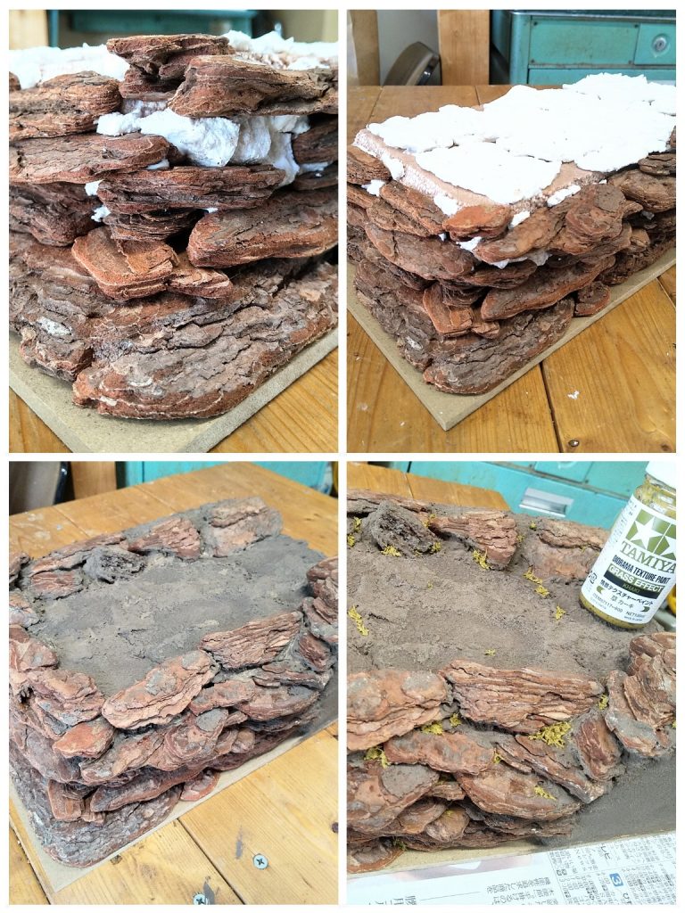 木工ボンドを塗って積み上げ、大きな隙間には紙粘土を。小さい隙間は土塗料を塗り込んで塞ぐ。上の地面も紙粘土。タミヤ テクスチャーペイントの「ダークアース」をベチョベチョ塗る。粘土は乾燥すると縮むので、一面繋げて覆うより、多少小分けにした方が良いかも。完成後も1ヶ月くらいはちょいちょい様子見して、縮んでいたら隙間を塗料で埋める。同じくテクスチャーペイントの「草 カーキ」を、岩(バークチップ)の隙間・土と岩の際・地面の亀裂等に乗せる。