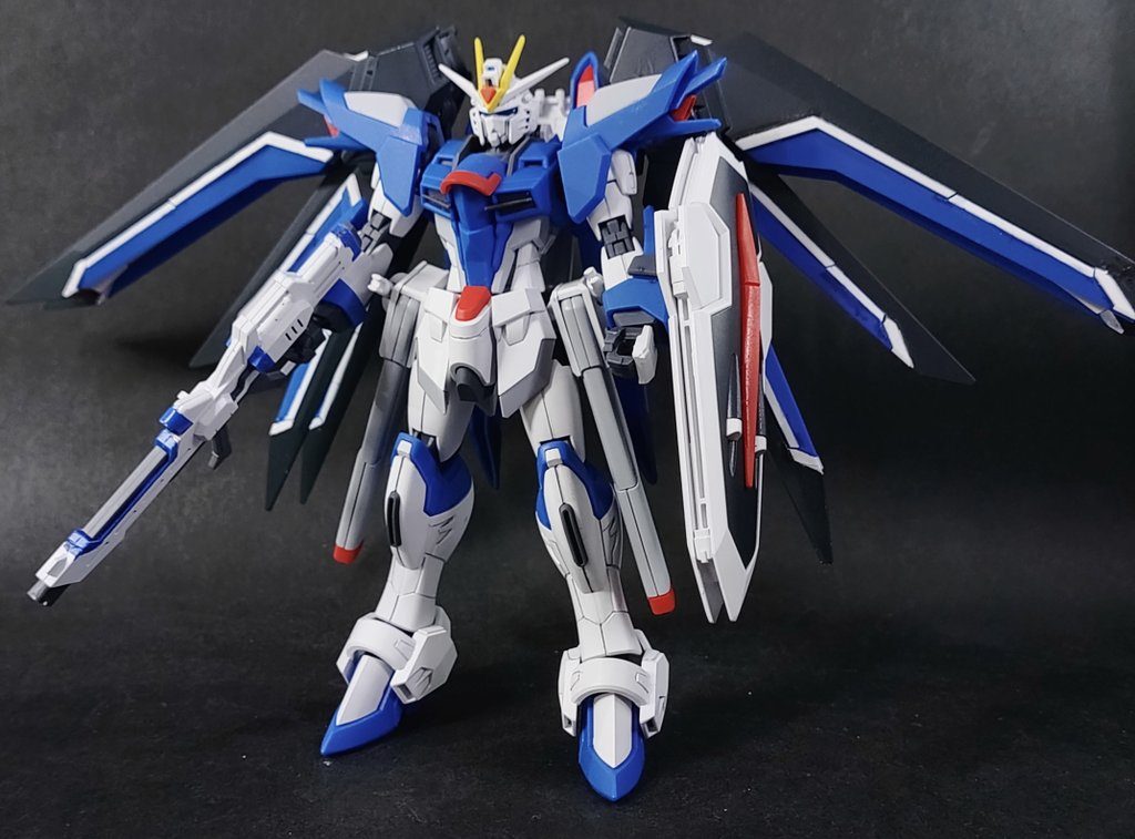 製作そのものはまさしくパチ組み。こどものニッパーEXとタミヤの薄刃先細ニッパーでバシバシ切り取ってアートナイフでゲート処理。スミ入れは0.5mmのシャーペンで行い、トップコートを拭いて完成です。ただこのキット、近年のHGにしてはシールが多いため敬遠される方もおられるようですね。特に翼の白ラインはすべてシールでの再現となっています。私は…根性で塗りました、ハイ。ダークブルーの部品は白サフ吹いてラインをキットのシールでマスキングし、その上からRGダブルオーダイバーアークの時に余ったネイビーブルーで上塗り。青い部品はガンダムマーカーのニューホワイトでラインを部分塗装して両者を組み合わせていますが…皆さん、素直にシール使った方がいいです。その方が数倍綺麗ですよ。頑張って塗ってもこの通りガタガタなので(´Д`)(というかキットの白ラインがかみ合わせ方式なので…)紙っぽさが気になるのであればシールそのものを塗装するのも手です。(なお、頭部やビームライフルのセンサー部のみシールに頼りました。後の部分は普通に塗装しています)