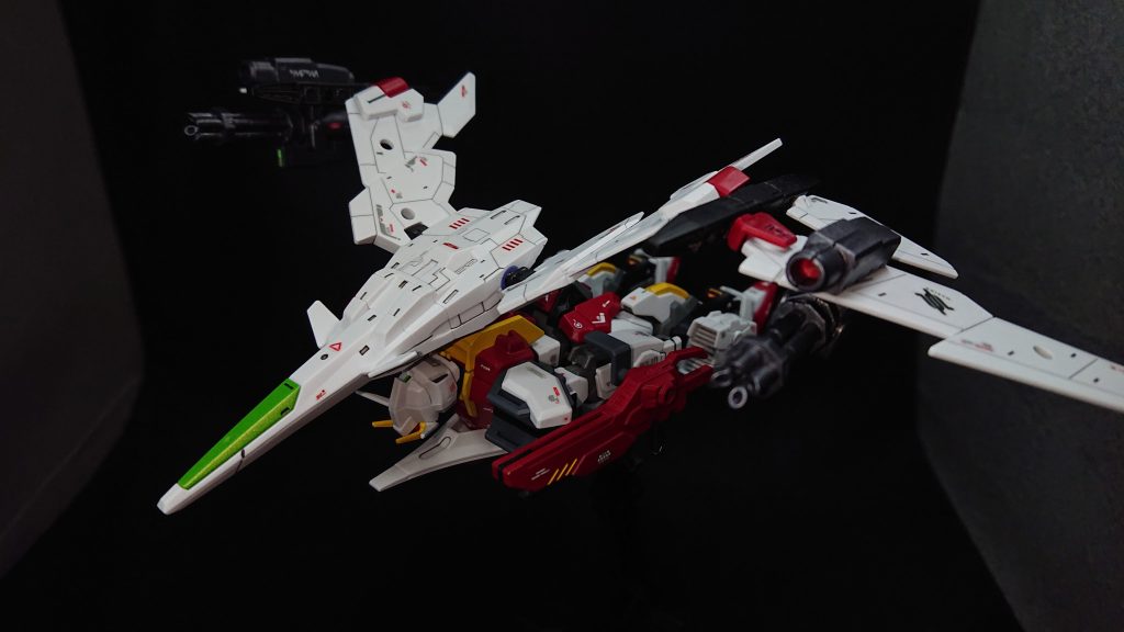 なんとか可変機構を組み込めないものかと考えた結果、簡単なモノではありますがSEED系の機体らしく最近話題の“寝そべり変形”で落ち着くことになりました飛行形態に変形するときは、最初に上半身を180度回転させ手足を真っ直ぐ伸ばします次にリアスカートのジョイント軸にシールドを接続、左腕のシールドのジョイント軸にビームライフルを接続しますバックパックのエグザビークルは180度回転させて機首を前方に向けます翼の先端部分が逆羽状態になっているので、黒いパーツの部分から動かし前方に向けます最後に脚部のスラスターやつま先、翼などの微調整を行い完成になります翼の位置が肩らへんにきているのでもう少し下げたかったのですが、そうなると機首の位置が微妙な感じになってしまうので、今回は機首の位置を優先しました「ファイヤージャンボ」のモチーフになったジャンボジェット機らしくはないのですが、今の自分の技量ではこれが精一杯でしたでも、デザインはなかなか気に入っていますw