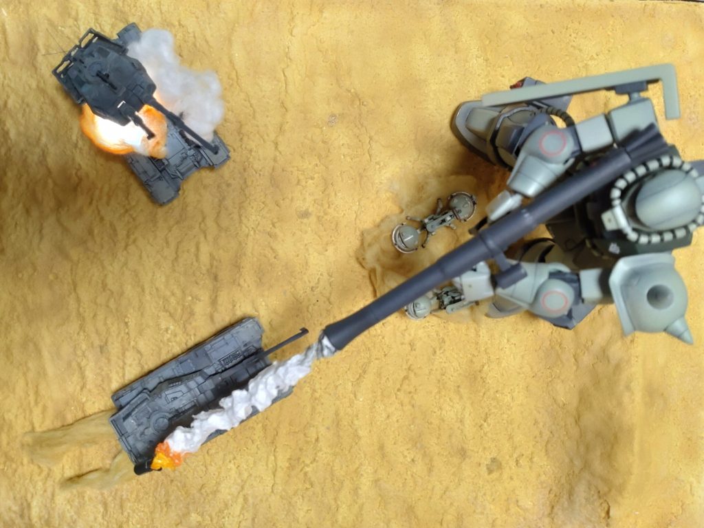 ジオラマのレイアウトは、こんな感じです。今回の一番の主役は、ザクバズーカーの砲弾です。これが、いかにジオラマの中央を横切るかで、戦場の緊張感が出るのでは無いかと思って、何パターンか試して決定しました。シャアズゴの時も作成した発泡スチロール製の煙ですが、今回倍以上長くしたので、保持するのが難しく、中に真鍮線を通してます。バズーカーから発射した弾丸が煙を残しながら、まっすぐ飛んで行く姿をイメージしました。ジオラマのベースは、発泡スチロールに紙粘土で砂丘を作成しました。そこに、水溶きボンドでティッシュを貼り付けて、RaMuShizuさんに教えて頂いた水溶きボンド＋重曹でベース作成が終了です。砂っぽい表現のところは、重曹を上からかけて、木工用ボンドとつや消しクリアで固着させてディティールを追加して、エアブラシ塗装しました。塗装後、剥がれないように、3回つや消しクリア吹いています。奥の61式戦車は、いつもの100均LED＋クリアオレンジで着色した脱脂綿で爆破しましたぁ！箱絵では、歩兵も活躍しているのですが、ザクに踏まれたり、61式に轢かれそうだったので、今回は出陣しませんでした。