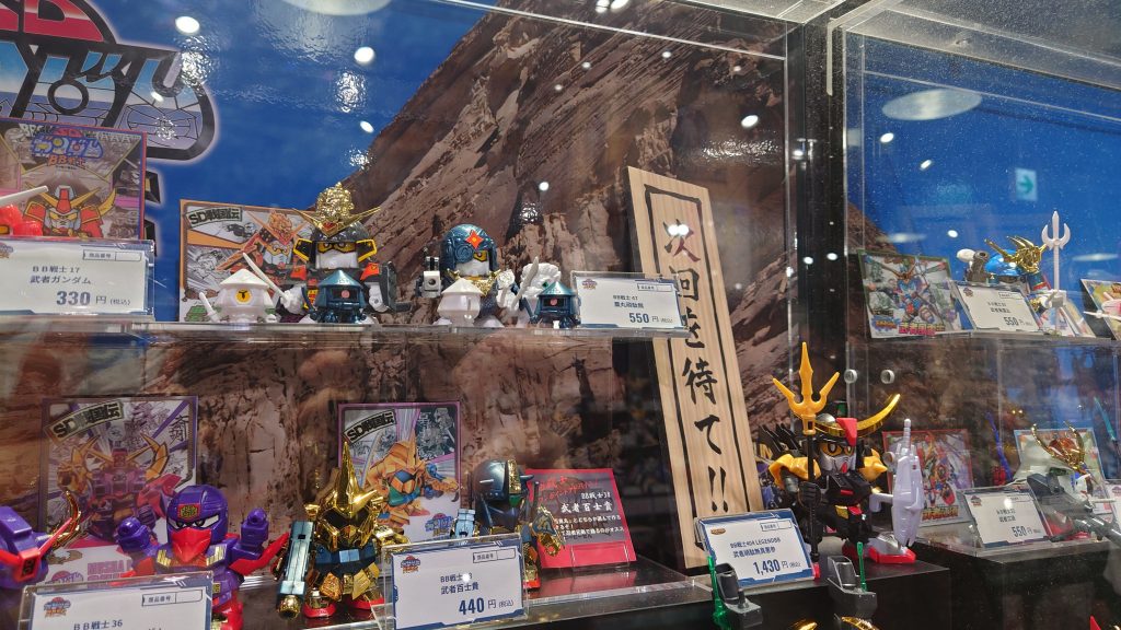 その次回を待て！が思いっきり掲示されてるのが今のガンダムベース東京（あの頃の武者の一部が再販中）。筆者です。'90年代前半頃のプラモデル（ガンプラ含む）、いろんな事を平行して考えるとなかなかに面白い展開。リアルガンプラにはまだＭＧすらなく、現在絶版の初代ＨＧが最高クラスで、世間がＳＤに傾いていた頃かぁ･･･これについてはいずれブログ「キッズプラモの興亡」にも。「GBNWeapons」は終了しましたが、懲りずにまたしても連作をやります。今回のテーマは「ＳＤのガンプラバトル」。「ＧＢＮＷ完結編」前後ではリアルガンプラのカスタムや色塗りに疲れ切り（ＳＤはＳＤで大変だけれど塗り面積は少ないので）、家の飾れるスペースも残りわずか（これは本当に死活問題）。自分がずっと大好きなＳＤで勝負です。