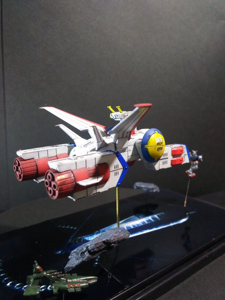 ベースは、ネットでスペースコロニーの写真を探し、印刷しベースに両面テープで貼り付けてあるだけです。ベースは100均のコレクションケースの台を使用。また、岩塊は100均の園芸用の木片チップをシタデルカラーの水色＋黒色の混色で筆塗り。後でシタデルカラーのシルバーでドライブラシをしました。ベースへの固定は銅線を使用しました。また隠れキャラとして「シャア専用ムサイ（ファルメル）」をホワイトベース下の岩塊の影に隠れて配置。距離的な関係やスケール等一致はしませんが・・・遊びの範疇です。このムサイは食玩の「マイクロフィギュアセレクション」の物を使用しました。（懐かしー）