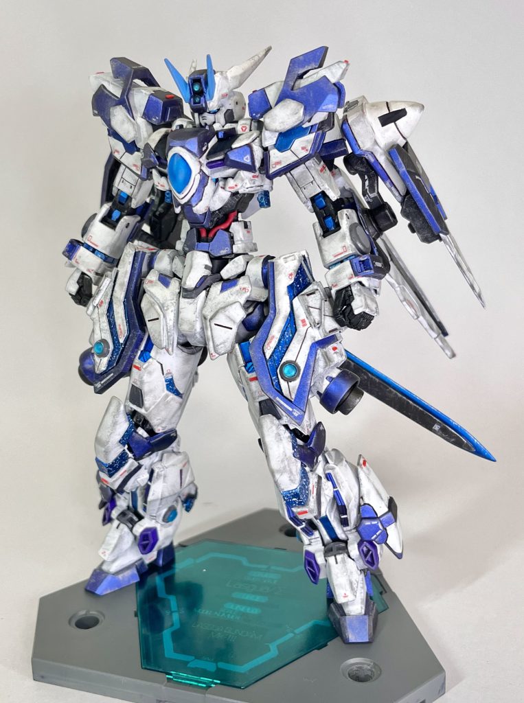 ラスグアガンダムMk-III型式番号[GNL-003Σ]コンセプトは｢3番目にして最強｣。来るべきGBN/メタバースに向けてMk-IIに続き新たに制作されたラスグアガンダム。青を基調としていたMk-IIに比べ、白い部分が多くなった。またMk-I、Mk-IIと比べて遥かに大型化しており、その大きさは宇宙世紀後半の機体であるシナンジュとほぼ同じ大きさである。大型化の理由は多くのシステムを取り入れたこと、人に近いフォルムに近づけたこと、どのガンダムともシルエットが被らないフォルムを目指したことによるもの。ありとあらゆるガンプラが組み合わさった結果、どの機体をベースにしたと言えば良いのか本人も分からないほど形状が変化している。ラスグアガンダムに共通した3基のGNドライヴに加え、機体各部にサイコフレームを取り入れることで反応速度と耐久性を強化し、ゼロシステムの搭載によってシステムの管理･特殊モード発動時の負荷軽減、最適化を計った。またサイコフレーム内部にGN粒子を流し込むことによって更なる強度と適応力を増加を狙った。加えてパーメットスコアとハロを組み合わせることで、ビット操作の正確性、機動力強化、情報処理補助などシステムが増えたにもかかわらず従来より機体そのものは扱いやすくなったと言える。GN粒子の色は先代機と共通して青であり、それに合わせてサイコフレームとパーメットシェルの色もデフォルトで青になっている。特徴的な大型サイドアーマーは脚部保護の他、サイコフレームの増設、大型スラスターの搭載によって移動速度と耐久度上昇に貢献している。背部にGNガンビット×4、腕部に内蔵型のGNビームサーベル、腰部後ろのGNハイパービームサーベルが標準装備されており、武器を持たずともある程度は戦闘を継続できるように最低限の武装は搭載されている。通常形態はこれに加え、GNガラティーン、GNロンゴミニアドという大型の剣と槍を扱う。尚後述する兵装によってはGNドライヴの数は更に増えることになり、Mk-Iの5基と同等もしくはそれ以上となる。