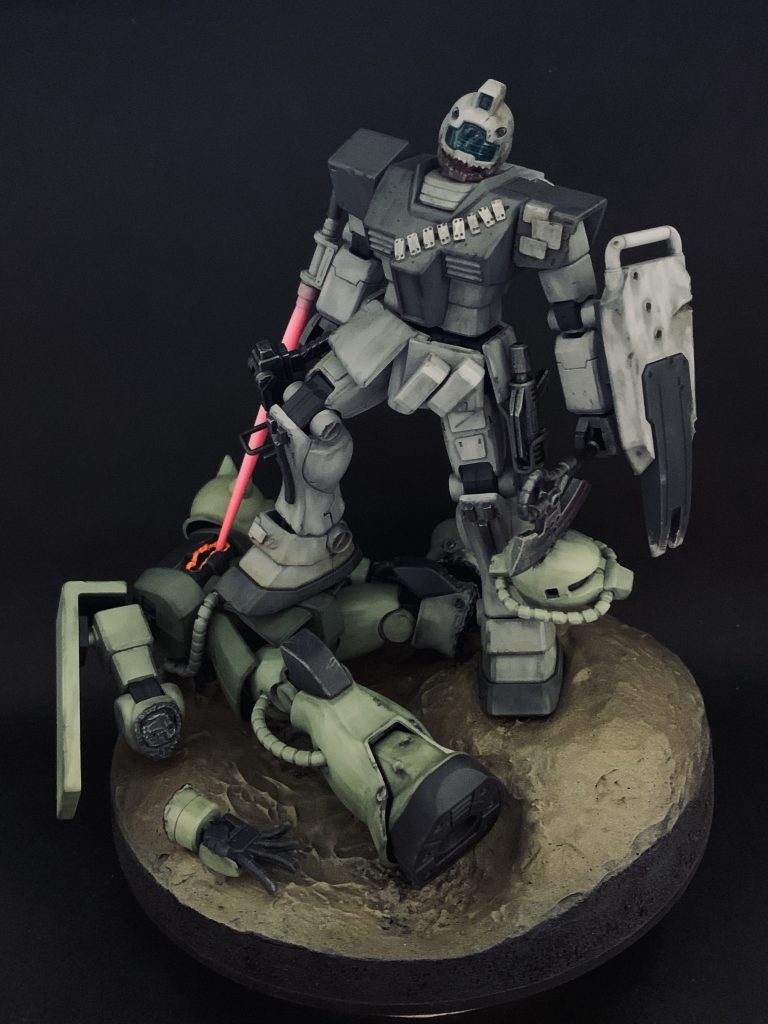 現在はザクと合わせたビネットで飾っています。HGジムは腰アーマーが邪魔で太ももを上げる動きが困難だったのでMG2.0の構造を真似て可動するようにしています。それでもあんまり太ももが上がらないので地面に段差をつけ、低いところにザクを置いて片足で踏み付けるポージングを成立させています。