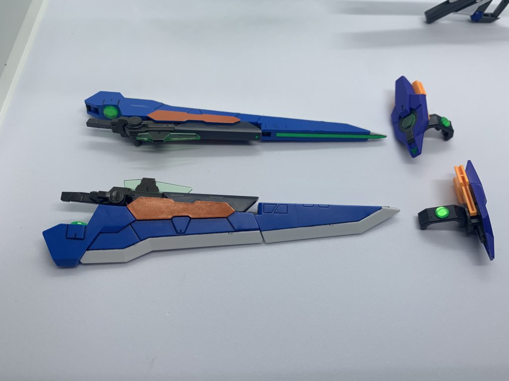 ・オリジナル武器、GNバスターソードビット・T。原型機のタクティカルアームズから大剣部分を持ってきて、ダイバーアーク付属のGNソード2のグリップ部分を接着剤で固定し、バーストレールガンの余ったレールを使ってカバーをしました。こちらも接着剤でくっつけてます。グリップ部分は干渉する部分をカットしましたが、レールカバーは加工なしで被せられました。グリップ下部にあった接続用の穴は、裏面にシャインシルバーを塗ったグリーンレンズを接着して隠し、GNコンデンサを表現しました。合体剣機能をオミットするにつき接続部分のカットと、3Dメタリックシールを貼り付けて穴隠しをしています。レールモードはこの穴隠しをしたときにピンときたもので、携行武器がレールガンなのもこのため。・アークブレイサー本体は加工なしそのままです。腕部接続用のコの字ジョイントは、レッドフレームのシールド接続ジョイントを加工しました。軸をカットし、切り口にバスターソードと同じくグリーンレンズを接着しコンデンサを表現。