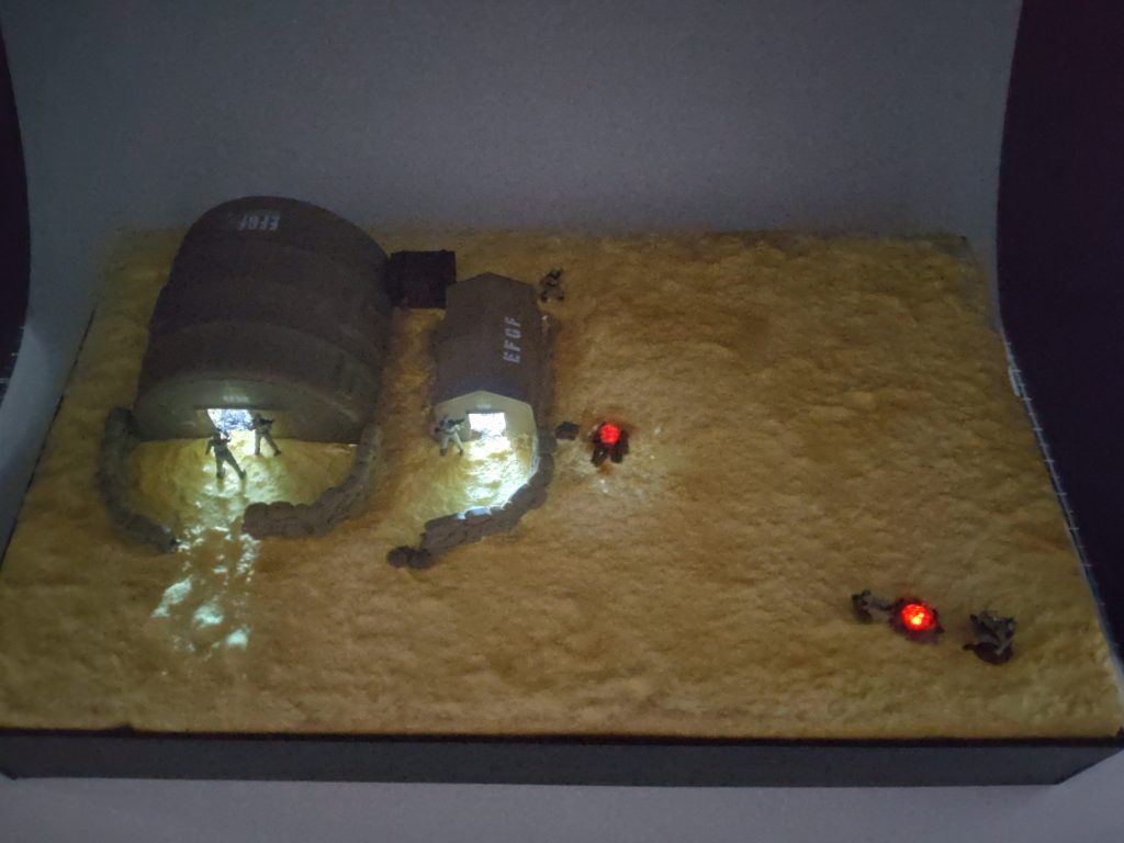 暗いところですと、こんな感じで光ってくれます。テントの中は、直接LEDを出したので、かなり明るいです。覗き込むと見えちゃいます。焚き火は、赤の透明ランナーの先をハンダでちょっと溶かして、炎っぽくしました。焚き火の回りは爪楊枝を薪割りして、燃やしてます。