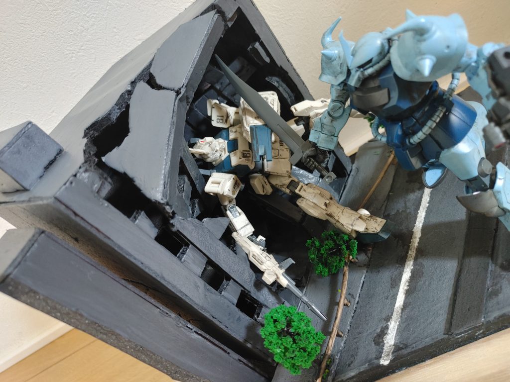 全体を引きでガンプラとウェザリングは普通に買いましたが、土台、地面、ビル、ジオラマの塗料すべて100均の材料、立木も100均です。ガードレールは、ランナーを汚して、曲げた物です。 