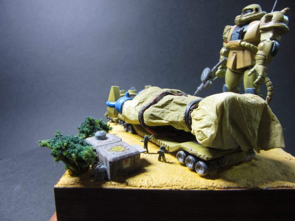 グフを覆っている幌はティッシュペーパーを黄色ぽく着色して、グフを包んでいます。バンドは輪ゴム。黒く塗りました。周りにいるジオン兵たち。これはアルミ線をひねって制作。ちょっといびつな感じの兵士たちです。ザクのコクピットも開孔。操縦士が手を振っています。