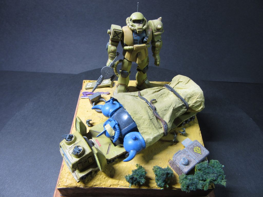 サムソントレーラーの運転車両上部の機銃はWLシリーズより。グフのモノアイカバーはマスキングテープを張り付けています。ベースはスチレンボードを切り出し積み重ね、木工用ボンドで固定。上から木粉ねんどで砂漠らしく地面を作り上げて塗装しています。外観は木目調テープで。