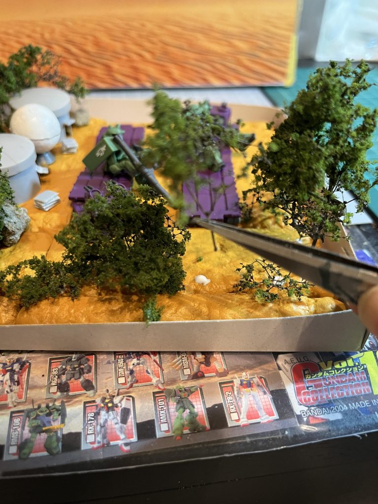 天然樹木を植林、石は庭から取得。地面はDAISOのレンガイエローです。箱はガンプラの箱。超低コスト。尖ったもので地面に穴を開けて木を植えてボンドで固定します。