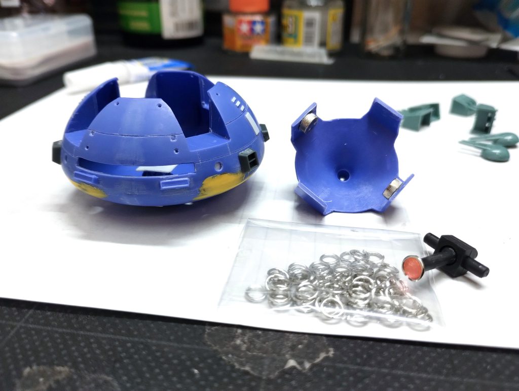 脚を切り取り、内部に可動できるモノアイを仕込みたかったので上部も切り取り蓋にしました。蓋はネオジム磁石で固定しているだけなので開閉可能。モノアイを好きな位置に動かせます。モノアイ自体はボールジョイントの先端にHアイズを取り付け、フチのメタル部分は100均で見つけた丸カンを接着。ボディに穴が空いてしまったところはポリパテで成形。元々ついている不要なモールドは接着剤埋めています。