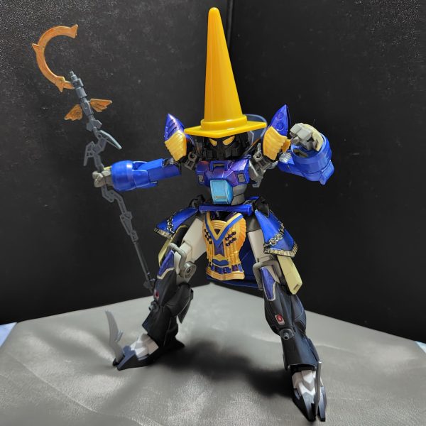 注）これはガンプラですよ……いやホント。デミトレーナーをメインにファイナルファンタジーシリーズの黒魔道士っぽいのを作っています。・肩アーマーや腰アーマーはクレオパトラキュベレイのを使用しています。・頭部はSDの部隊兵を使用し、そこに100均ショップで買ったカラーコーンを被せてます。※多少頭部を削るなどの加工をしています。・脚部はフェイクニューユニットの脚パーツを使ってます。※この部分は地味にいつものデミトレーナーの脚に換装できたりします。・杖は30MMの魔法セットを使ってます。この黒魔道士は最終的にFFⅨの黒のワルツ3号みたいに仕上げるつもりです。その為に、バックパックに翼パーツを装着できるようにするところです。（2枚目）