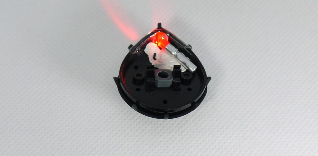 モノアイ発光ですが、まずはモノアイの位置に穴を開けます。そこにWAVEのＨ・アイズ（ピンク）を裏側からセロハンテープで貼り付けます。その後ろにミライトを「ひっつき虫」（コクヨのソフト粘着剤）で固定してやりました。