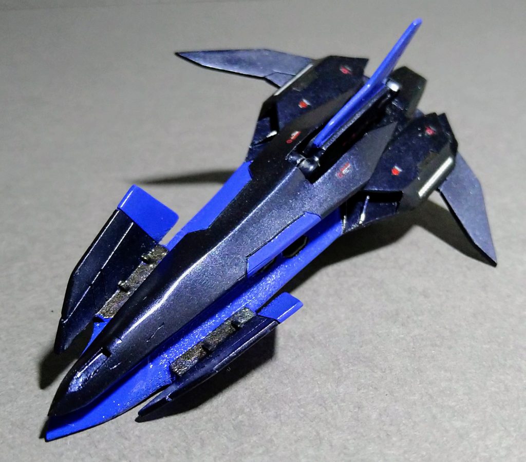 ゴースト本体で上側からの姿になります。特徴は本体に被さるように搭載されている大型GNビームライフルでメイン武装として使用されます。本体とライフルを繋げるアームは縦型尾翼と統一させることで空力抵抗を軽減させています。無人のため安定性を重要視しなくても良い事から主翼は小さくして軽量化を図り旋回性が高い前進翼を採用しています。