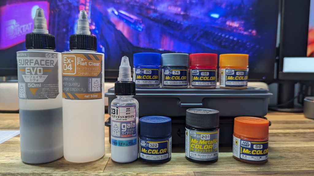 塗装レシピは以下のとおりです。下地:ガイア サーフェイサーエヴォフレーム:クレオス GXメタルブラックボディ:ガイア アルティメットホワイト(オリジナル調色)ボディ青:クレオス コバルトブルーボディ水色:クレオス エアスペリオリティーブルーバックパック:クレオス オレンジアクセント①赤:クレオス スーパーイタリアンレッドアクセント②黄:クレオス キャラクターイエローアクセント③蛍光:水性 クレオス 蛍光グリーンアクセント④金:水性 タミヤ チタンゴールドトップコート:ガイア EX04フラットクリアー前作に引き続きGXメタルブラックをフレームや武器に使用。今回はボディの白を「若干の青系統」にすべく、フタロシアニンブルーを1~2%程度調色したものを使いました(画像中央の小型ボトル)。ほんとーに、ごく僅かに青っぽくなり、クールさが出たと思います。