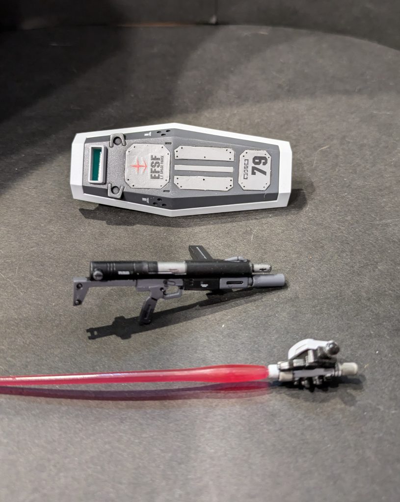 装備類マシンガンはストックの腕への干渉がキツく、無理がある感じでしたのでグリップの位置を2ミリ下げました。持ち手と一体成型のビームサーベルはクリアパーツに変更、マスキングベタベタで塗り分け。シールドはプラ板による追加装甲、覗き窓へのクリアパーツ追加を行っています。