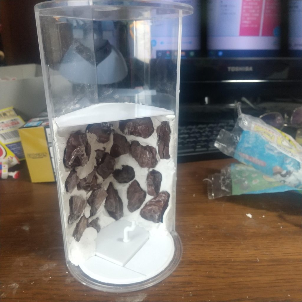 100均でディスプレイケース、紙粘土、プラバン、バークを購入。ガンプラくんの台座も床に埋め込み、ポーズを固定しやすいように。下半分はむき出しの岩肌を作るために紙粘土を張り付けてバークを埋め込む。