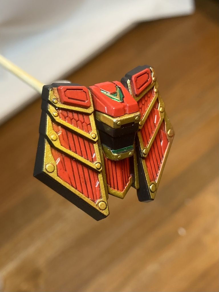 フロントアーマーを例に塗装の手順を。①スターブライトゴールド(ラッカー)→クリアイエロー(ラッカー)でキャンディー調に塗装②モンザレッド(水性)で塗装→マジックリンでゴールド部分を拭き取る→クリア(ラッカー)でコート③調色した黒(水性)で塗装→マジックリンで不要な塗装を落とす。※②でクリア(ラッカー)をコートしているのでモンザレッド(水性)はマジックリンで拭き取っても落ちないで残ります。④ブラック(エナメル)でスミ入れ⑤つや消し(水性)でコート→ゴールドの部分だけマジックリンで落とす。これでゴールドだけ艶ありになります。⑥グリーンはキットに付属のシールをカットして貼って、エナメル塗料のクリアを筆塗りでコートしています。