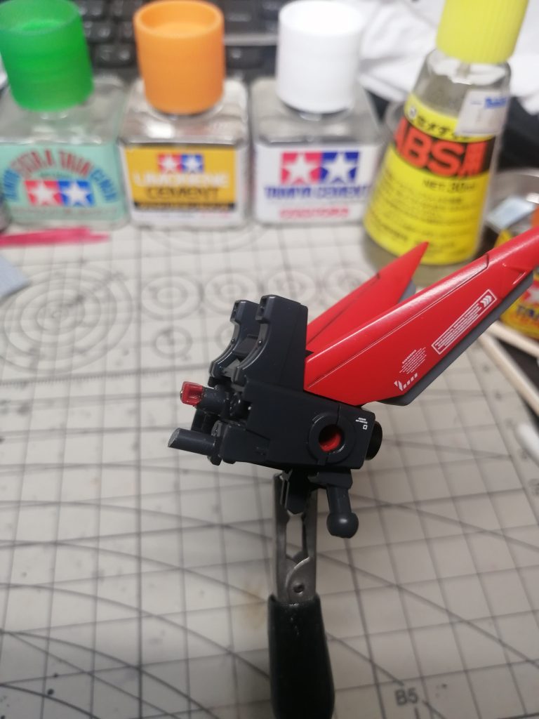 フライトユニットはRGレッドフレームには無改造では接続できないので、色々手を加えて接続できるようにしました。 まず、フライトユニットの先端の3mmジョイント部分を切り落として、この赤い四角のパーツを接着。この赤いパーツは、以前製作したRGレッドフレームのバックパック接続ジョイント先端を切り離したものです。これをフライトユニット3mmジョイントを切り離したところに接着し、ピンバイスで1mmの穴を空けて真鍮線を差し込みます。これだけじゃ心許ないので、少し下に余ったランナーの切れ端を接着しました。支柱みたいな感じの役割です。