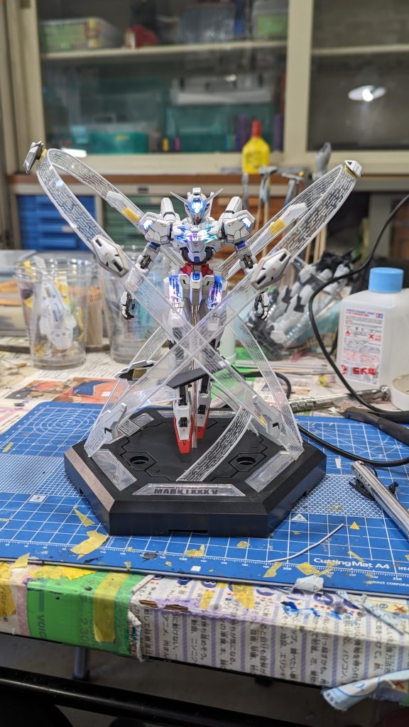 台座を用意しビットを周りに飛ばした図。股の3ミリ穴に透明パイプを刺し、そこに導線を通しました。台座は御模堂のアイアンマンMark85のものから流用していて、この下にESP32が収められています。ビットはダイソーのプラ板とワイヤーを組み合わせたものの上にマグネットによって固定されています。ビットは肉抜き穴埋め、マグネット埋め込みの処理が行われています。プラ板にはケガキによってパーメット柄が彫られています。